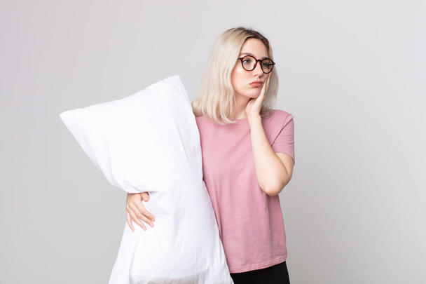 young pretty albino woman feeling bored, frustrated and sleepy after a tiresome wearing pajamas and holding a pillow - Photo, image