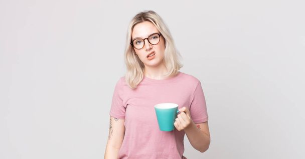 young pretty albino woman feeling puzzled and confused with a coffee mug - 写真・画像