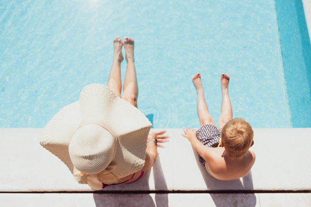 Young mother with son taking sun and sitting on the edge of the swimming pool - Photo, Image