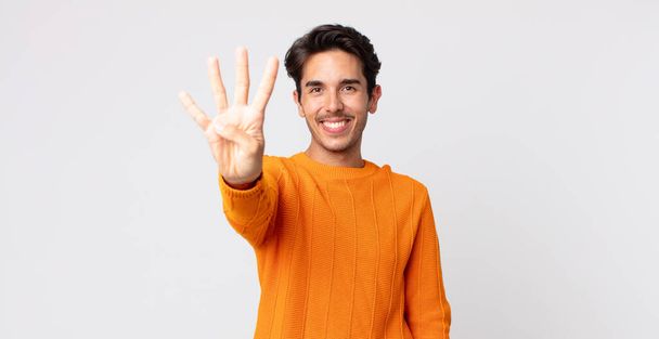 hispanic handsome man smiling and looking friendly, showing number four or fourth with hand forward, counting down - Foto, afbeelding