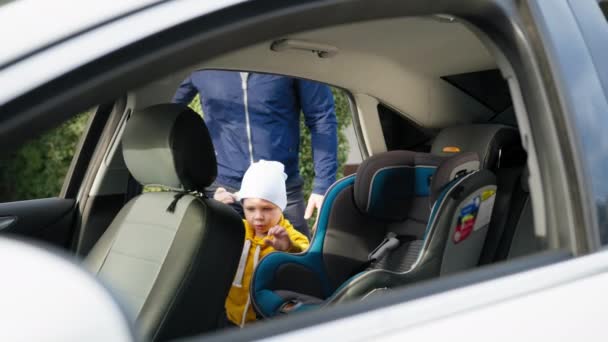 безпечна дитина, чоловік батько кладе свого сина на заднє сидіння на дитяче автокрісло і кріпиться ременями безпеки під час спільної поїздки з дитиною
 - Кадри, відео