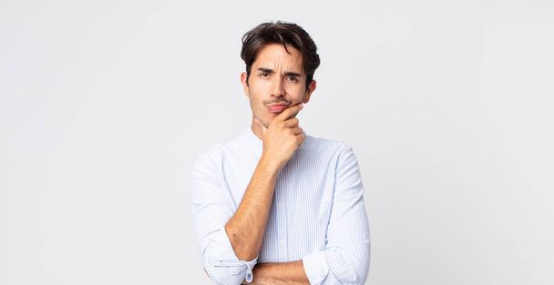hispanic handsome man looking serious, thoughtful and distrustful, with one arm crossed and hand on chin, weighting options - Fotoğraf, Görsel
