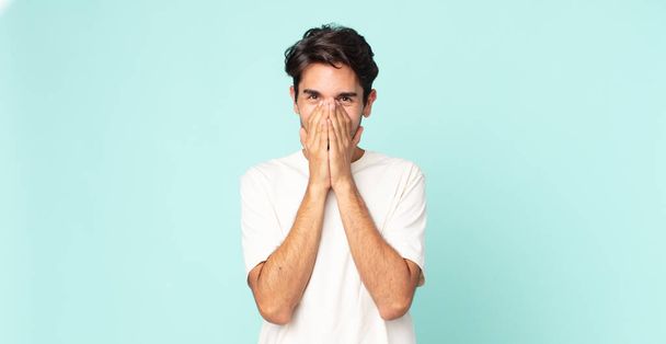 hispanic handsome man looking happy, cheerful, lucky and surprised covering mouth with both hands - Foto, afbeelding