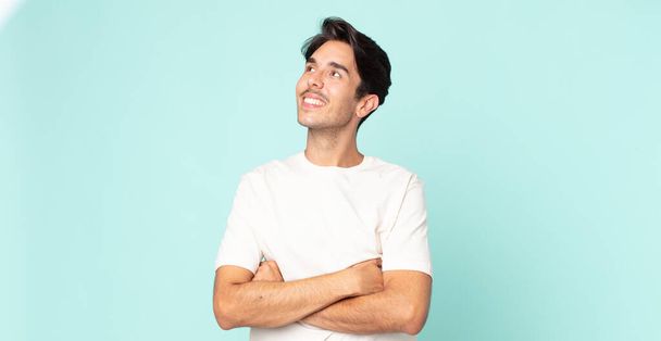 hispanic handsome man feeling happy, proud and hopeful, wondering or thinking, looking up to copy space with crossed arms - Photo, image