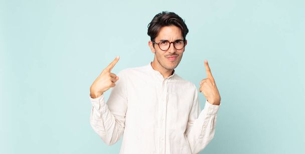 hispanic handsome man with a bad attitude looking proud and aggressive, pointing upwards or making fun sign with hands - Photo, image