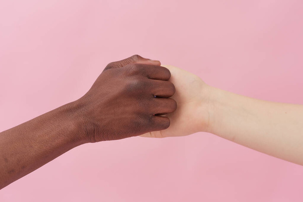 Une poignée de main entre un homme afro-américain et une femme caucasienne posant sur un fond rose, se saluant, démontrant les relations internationales. Gros plan. Poignée de main - Photo, image