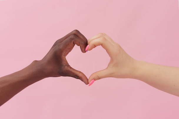 Biała kobieta i Afroamerykanin pokazują serce z rękami na różowym tle. Koncepcja rasizmu, tolerancji - Zdjęcie, obraz