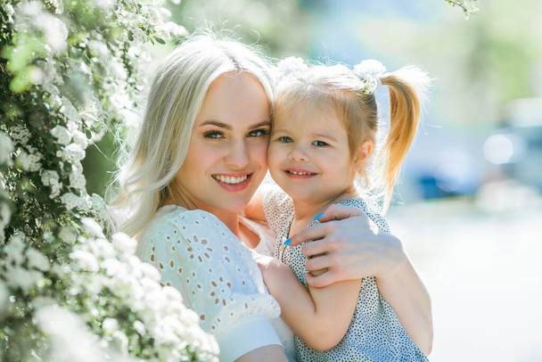 A beautiful young mother with her daughter 3 years old in a blooming garden. Spring. - Photo, Image