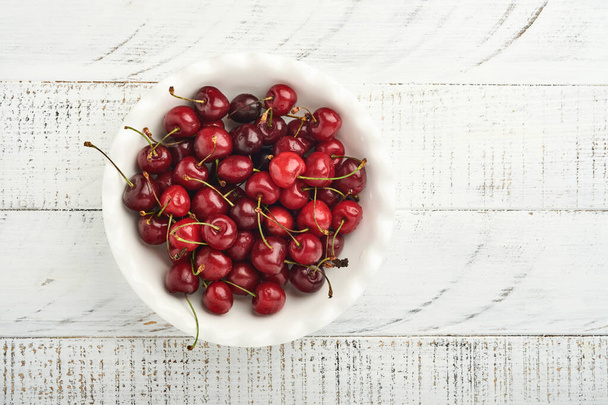 Cherry with water drops on white bowl on white stone table. Fresh ripe cherries. Sweet red cherries. Top view. Rustic style. Fruit Background - Fotografie, Obrázek