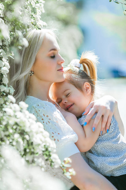 Una hermosa madre joven con su hija de 3 años en un jardín floreciente. Primavera. - Foto, imagen