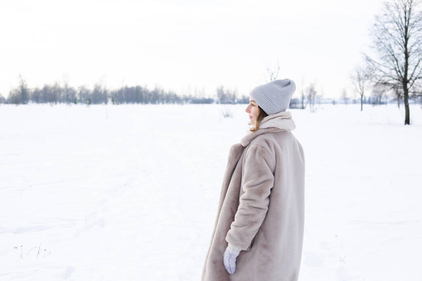 Junges Mädchen in beiger Kleidung, Pelzmantel aus Kunstpelz geht im Winter spazieren - Foto, Bild