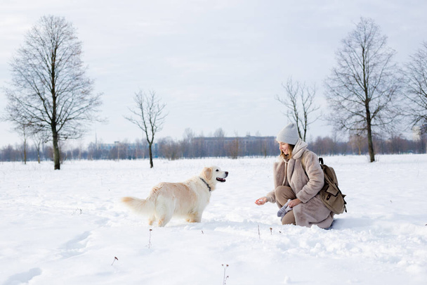 Jonge mooie vrouw en haar golden retriever hond hebben plezier in de winter. - Foto, afbeelding