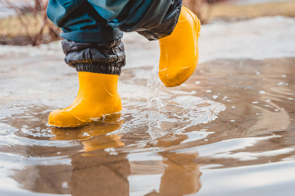Os pés de uma criança em botas de borracha pisam através de poças - Foto, Imagem