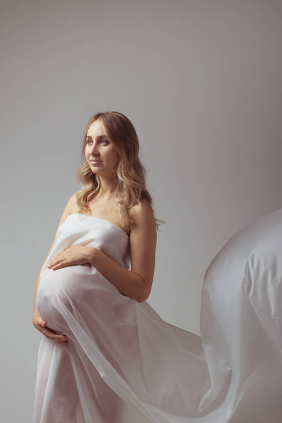 Mujer joven embarazada elegante de pie usando tela ligera. Concepto de embarazo, fantasía y cuento de hadas. - Foto, imagen
