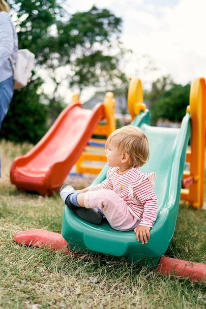 Kind sitzt auf einer Kinderrutsche auf dem Spielplatz. Seitenansicht - Foto, Bild