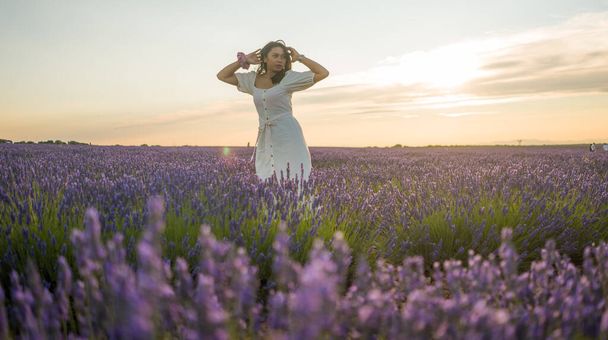 outdoors romantic portrait of young happy and attractive woman in white summer dress enjoying carefree at beautiful lavender flowers field in travel and holiday concept - Фото, изображение