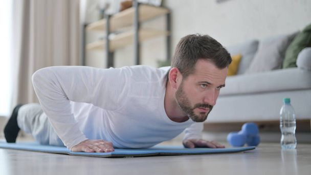 Крупный план зрелого взрослого человека, делающего отжимания на ковриках для йоги дома - Фото, изображение