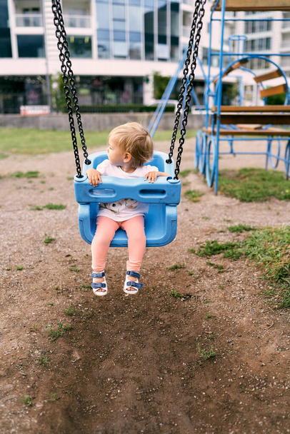 Klein meisje zittend op een schommel in de speeltuin, haar hoofd naar achteren draaiend - Foto, afbeelding