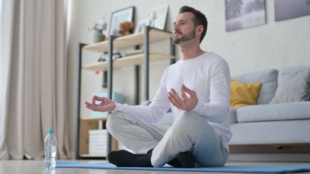 Uomo adulto maturo che medita sul tappetino da yoga a casa - Foto, immagini