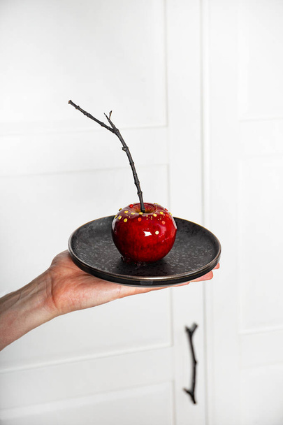 Red apple in caramel with sugar decor, an original treat for a festive Halloween table, vertical photo - Foto, imagen