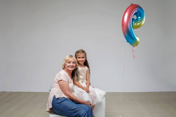 Chica con el pelo largo en vestido festivo con su abuela mayor, fondo blanco, familia, toma de estudio - Foto, imagen