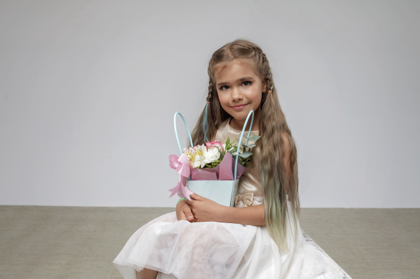 Girl with long hair in festive dress holds and scents bouquet of flowers, white background, studio - Photo, Image