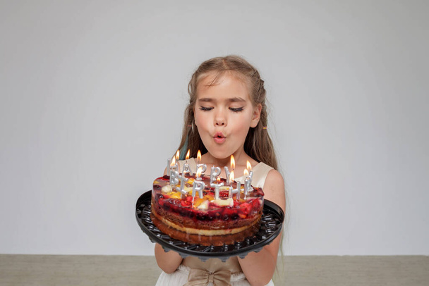 Girl in festive dress holds birthday cake with candles, white background, birthday celebration - Foto, immagini