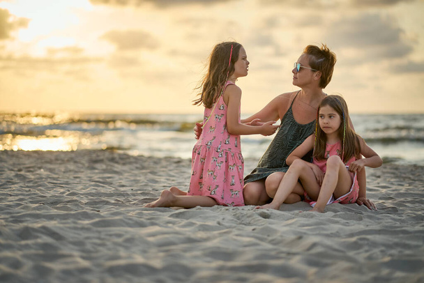 Νεαρή ευτυχισμένη όμορφη μητέρα και οι κόρες της στην παραλία το ηλιοβασίλεμα.  - Φωτογραφία, εικόνα
