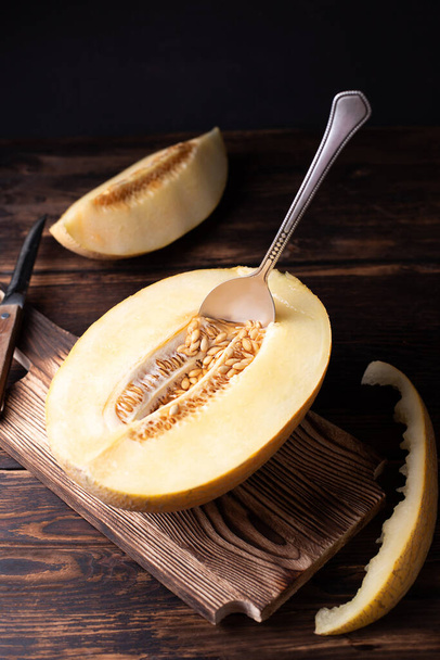 Half ripe melon with seeds and spoon on cutting board on dark wooden background, rustic style. - Foto, Imagem