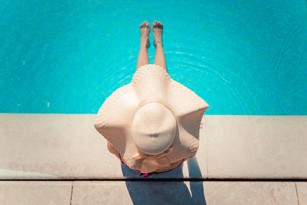 Niepoznawalna młoda kobieta w wielkim kapeluszu relaksująca się w basenie w kurorcie spa. Koncepcja relaksu - Zdjęcie, obraz