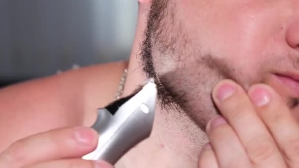 Acercamiento de un hombre afeitándose la barba en la cara con una navaja eléctrica. - Metraje, vídeo
