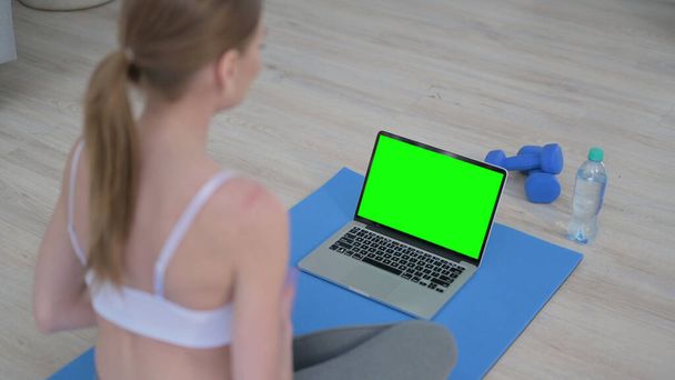 Vista trasera de la mujer haciendo yoga mientras mira el ordenador portátil con pantalla clave de croma  - Foto, imagen