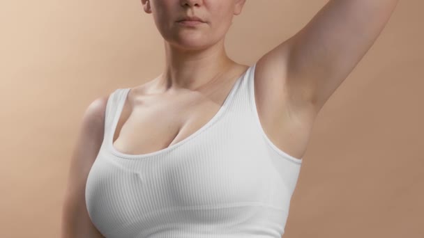 Blanke anonieme jonge vrouw in witte top die deodorant spuit op haar onderarm. Studio slow motion video op beige achtergrond. - Video