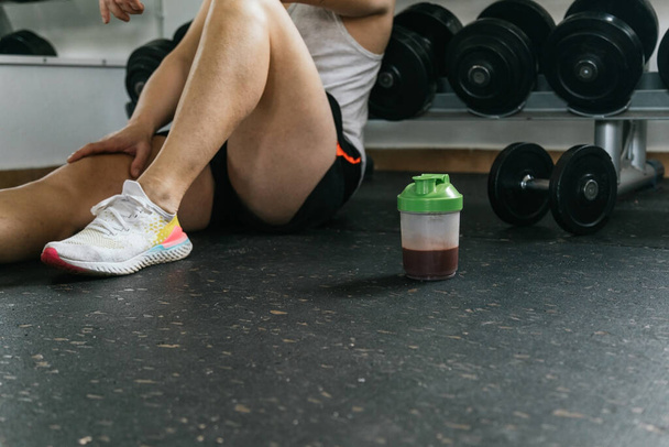Man sitting with a Smoothie in the gym. Post workout. Chocolate protein shake. Athlete builder muscles lifestyle - Fotoğraf, Görsel