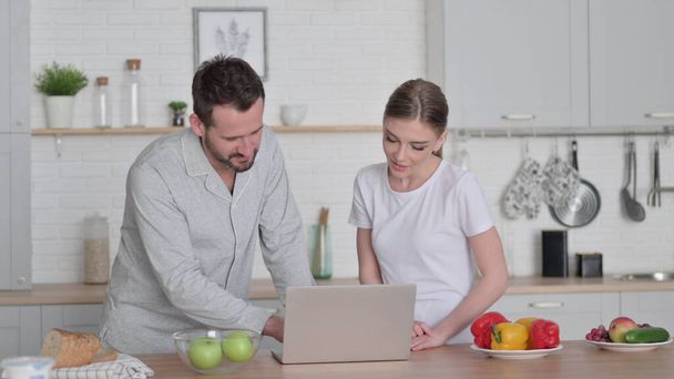 Женщина и мужчина работают над ноутбуком на кухне - Фото, изображение
