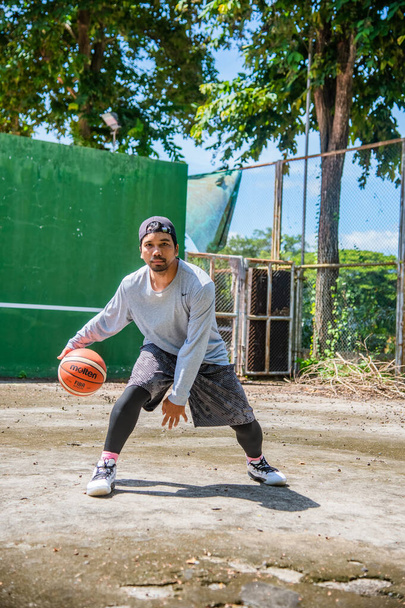 Man die buiten traint in de zon door basketbal te spelen tijdens de COVID-19 crisis, 26 juni 2021, Surat Thani, Thailand. - Foto, afbeelding