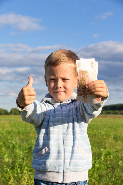 Tyytyväinen esikoululainen lapsi villapaidassa pitää paperiruplaa luonnossa pellolla sinisen taivaan taustalla pilvillä. Lähemmäs. Muotokuva - Valokuva, kuva