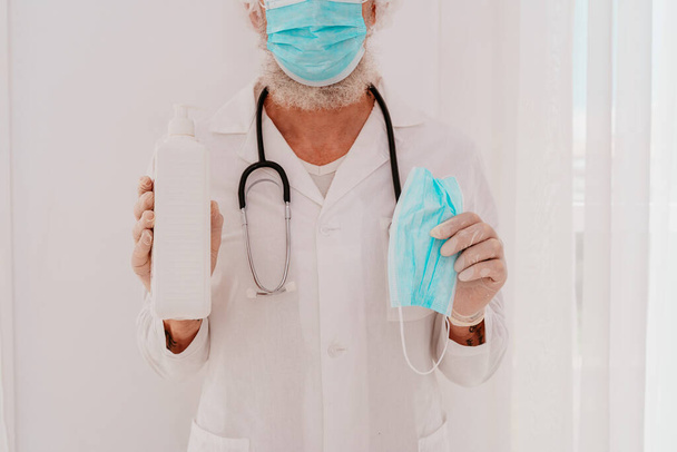 Doctor shows a disinfectant gel and a face mask for covid-19 virus - Photo, Image