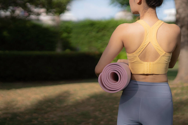 Crop Frau dreht sich um, hält rosa Roll Yogamatte an der Taille und schaut weg, dicke, weiche und süße Farbe Yogamatte mit guter Übung und guter Körperform. - Foto, Bild