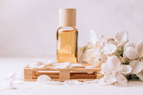 Olio cosmetico, aromatico o massaggiante su podio in legno sotto forma di pallet su superficie in gesso leggero con fiori di mela - Foto, immagini
