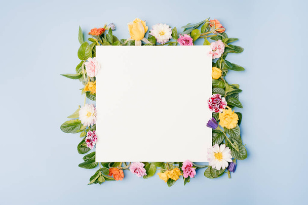 Blank paper card with square floral frame of assorted flowers on blue pastel background. Top view mockup with copy space. - Foto, Imagem