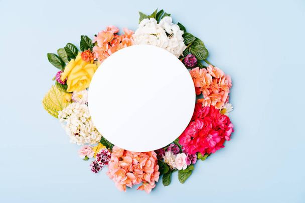Tarjeta de papel en blanco con marco floral redondo de flores mixtas sobre un fondo azul pastel. Vista superior del modelo con espacio de copia. - Foto, Imagen