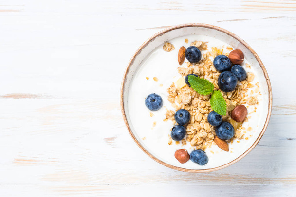 Joghurt-Müsli mit frischen Blaubeeren auf weißem Holztisch. - Foto, Bild
