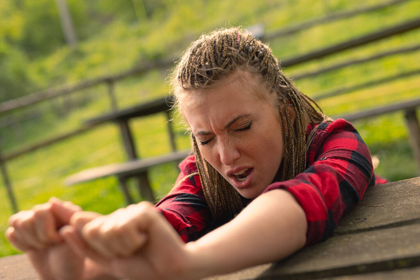 mujer joven se estira extendiendo los brazos sobre una mesa de madera áspera en un parque público, está somnolienta o cansada o necesita oxígeno como cualquier persona bosteza - Foto, Imagen
