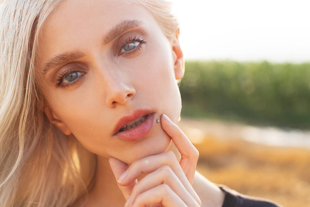 Close-up portret młodej ładnej blondynki z niebieskimi oczami, w terenie. - Zdjęcie, obraz