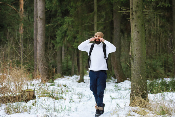 Szabadtéri portré egy jóképű férfiről kabátban és skorpióban. Szakállas férfi a téli erdőben. - Fotó, kép