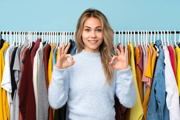 Έφηβη Ρωσίδα που αγοράζει ρούχα που είναι απομονωμένα σε μπλε φόντο και δείχνουν μια πινακίδα με δάχτυλα. - Φωτογραφία, εικόνα