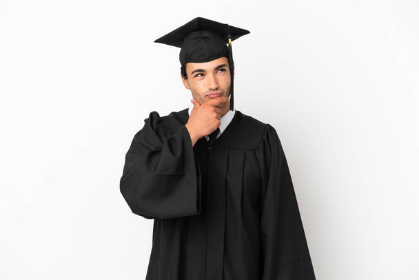 Mladý vysokoškolský absolvent nad izolovaným bílým pozadím s pochybnostmi a zmateným výrazem - Fotografie, Obrázek