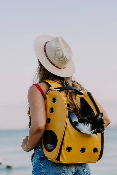 young woman with a cat in a backpack on the seashore. Travel concept with a pet. - Foto, Imagem
