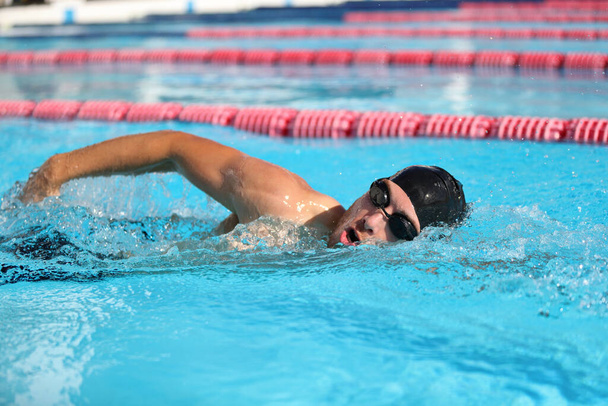 Swim competition swimmer athlete doing crawl stroke in swimming pool. Sports man male swimmer with goggles and cap breathing racing in indoor stadium. Speed exercise workout - 写真・画像